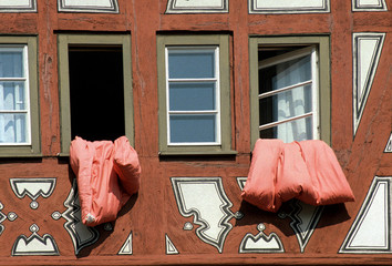 rote Bettwäsche hängt zum Lüften aus einem Fenster im Fachwerkhaus