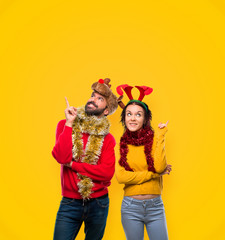 Couple dressed up for the christmas holidays pointing with the finger a great idea and looking up on yellow background