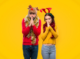 Couple dressed up for the christmas holidays keeps palm together. Person asks for something on yellow background