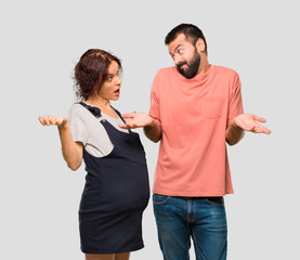 Couple with pregnant woman having doubts and with confuse face expression on isolated grey background