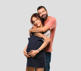 Couple with pregnant woman hugging on isolated grey background