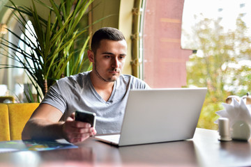 young guy is freelancer in cafe working behind laptop