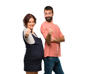 Couple with pregnant woman giving a thumbs up gesture and smiling on isolated white background