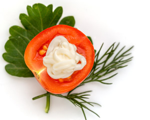 A half of red cherry tomato with parsley, dill and mayonnaise, on a white background.
