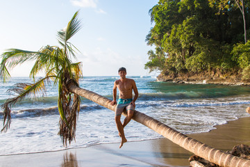 Obraz premium Junger sportlicher Mann sitzt auf einer Palme in Costa Rica am Strand