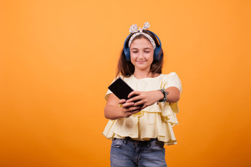 Little girl with yellow t-shirt listening music from her phone and headset. Joyfull gil