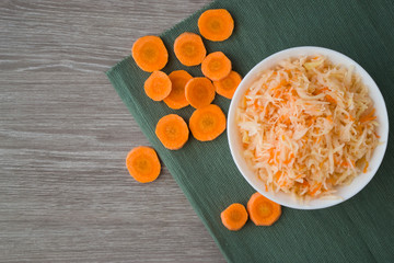 Photo cabbage and carrot salad in a plate on a dark turquoise napkin and a wooden table.