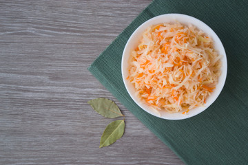 Photo cabbage and carrot salad in a plate on a dark green napkin and a wooden table.