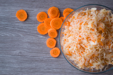 Salted chopped cabbage with carrots in a Cup on a wooden background.