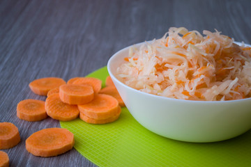 Photo Orange pieces of carrots and cabbage salad and carrots in a plate on a green napkin and a wooden table.
