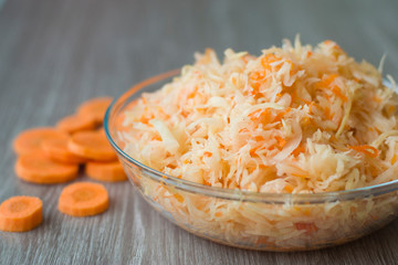 Salted chopped cabbage with carrots in a plate and Orange pieces of carrots on a wooden background.