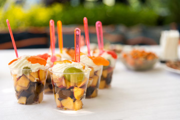 Catering for party. Close up of appetizers with peaches, plums, grapes and cream in short glasses on white table.
