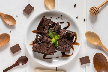 A plate of brownies with chocolate sauce on white wooden background, mint leaf on top, top view