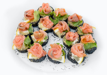 Close up of small canapes arranged on a plate over light background - selective focus