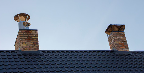 Brick smoke on the roof with metal roofing, green color, against a clear sky