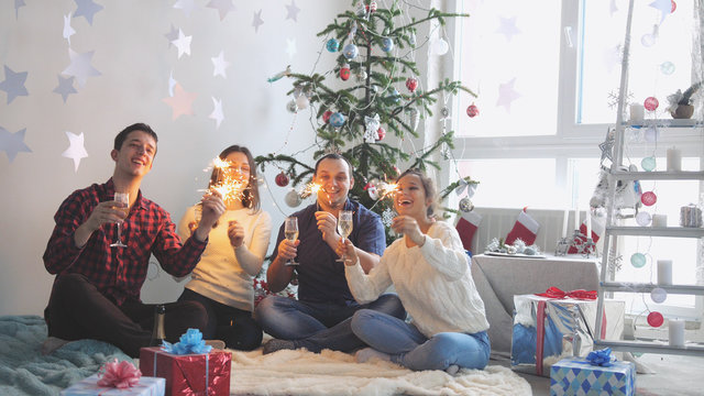 Happy young friends drink champagne and burn sparklers during celebrate New Year or Christmas Eve