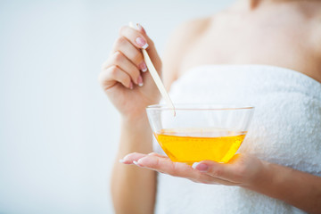 Women hold orange paraffin wax bowl. Woman in beauty salon