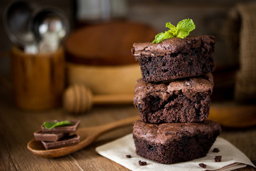 A stack of chocolate brownies on wooden background with mint leaf on top, homemade bakery and...