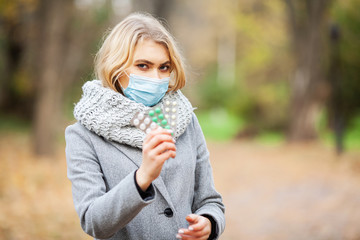 Cold and flu. Woman in autumn park holding pills