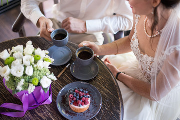 Fototapeta na wymiar Hands of young couple eating cakes with coffee on wooden table with gift box and flowers.