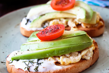 Toasts with avocado pieces, cherry tomatoes, scrambled eggs and soft cream cheese.