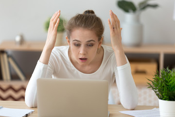Upset young female looking at laptop screen shocked experience virus attack, frustrated girl read breaking news online at computer at home, surprised woman get unexpected email or notice