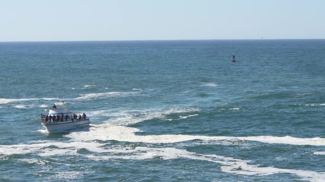 A whale watching boat coming in near Depoe bay, crowded with tourists, a buoy in the background.