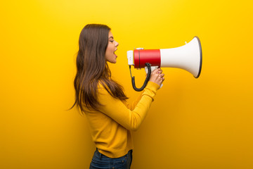 Teenager girl on vibrant yellow background shouting through a megaphone to announce something in...