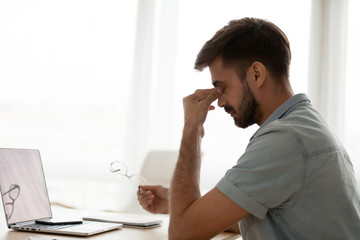 Exhausted man worker massage nose bridge suffer from dizziness or blurry vision, tired male take...