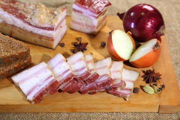 Smoked bacon, sliced on a wooden plank. Smoked bacon, red onion, salt and pepper on a clay dish. Smoked lard.