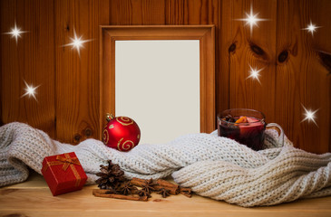 Empty wooden frame, glass of mulled wine wrapped in scarf, christmas ball, gift and spices. View with copy space.