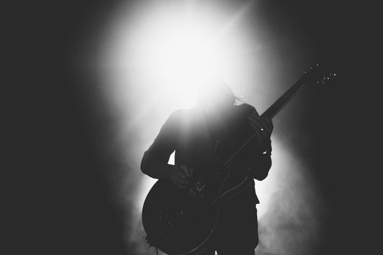 Black and white picture of guitarist silhouette playing solo in bright backlights 