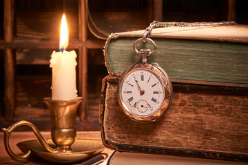 Alte Büchher mit Uhr bei Kerzenlicht