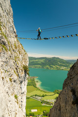 Climber walking on a high bridge on Drachenwand via ferrata above lake Mondsee, Austria