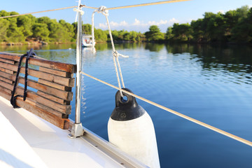 Obraz premium The deck on a sailing yacht and finger against the backdrop of a picturesque green bay with a yacht anchored. Outfit of a sailing yacht. Maritime practice of the yacht school.