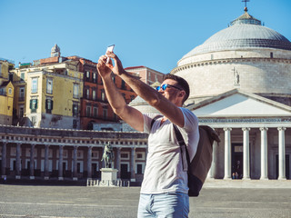 Handsome man with a phone on the background of the square and the old palace in the beautiful city of Naples, Italy. Technology and travel concept