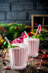 Christmas sweet cold drink, Homemade Peppermint Candy Cane Milkshake in two glasses, old wooden background with xmas decorations copy space