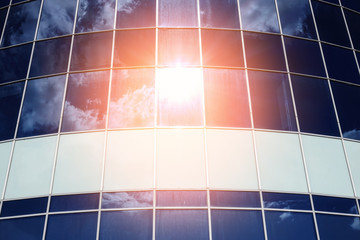 sun, blue sky and clouds are reflected in the glass by the modern facade