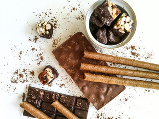 Different varieties of chocolate, chocolate tubes and cocoa on a white table