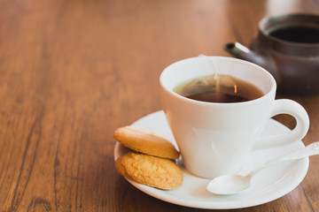 A tea cup with cookies on wooden table and copy space.
