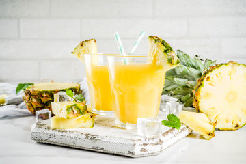 Fresh pineapple juice or cocktail, with pieces of fresh pineapple, ice, decorated with mint, on a white marble table, copy space