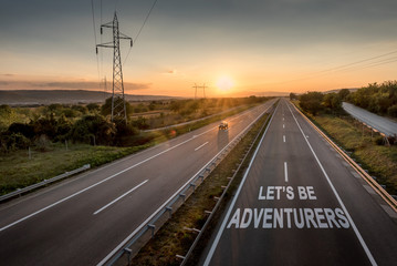 Fototapeta premium Beautiful Countryside Motorway with a Single Car at sunset with motivational message Let's Be Adventureus