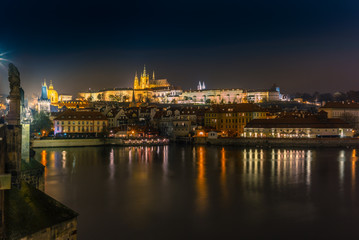 Fototapeta na wymiar View f the skyline of Prague's castle and the riverside buildings and street lights reflecting on the Vltava river in a cold winter night