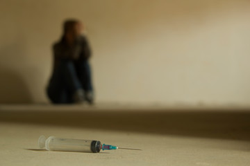 Drug addiction teenager sitting on the cement floor with syringe foreground