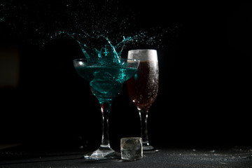 The breaking of a glass with fragments. The explosion of a glass on a black background with a colored liquid. Splashes of colors.