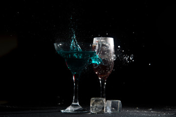 The breaking of a glass with fragments. The explosion of a glass on a black background with a colored liquid. Splashes of colors.