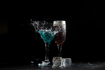 The breaking of a glass with fragments. The explosion of a glass on a black background with a colored liquid. Splashes of colors.