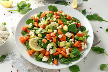 Avocado, roasted sweet potato, spinach, feta cheese healthy salad in white plate.