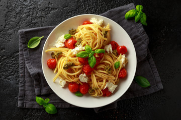 Pasta with green pesto sauce, roasted cherry tomatoes and mozzarella cheese in white plate on dark rustic background