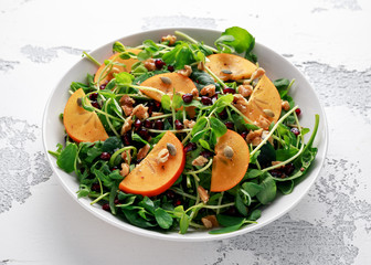 Persimmon and pea shoot salad with walnuts, pomegranate and pumpkin seed in a white table
